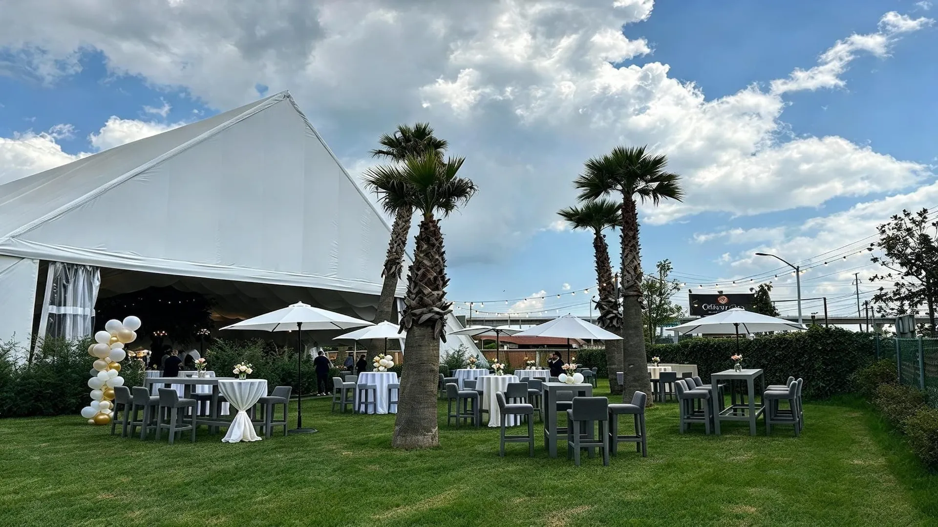 Jardín con mesas altas y palmeras para eventos al aire libre